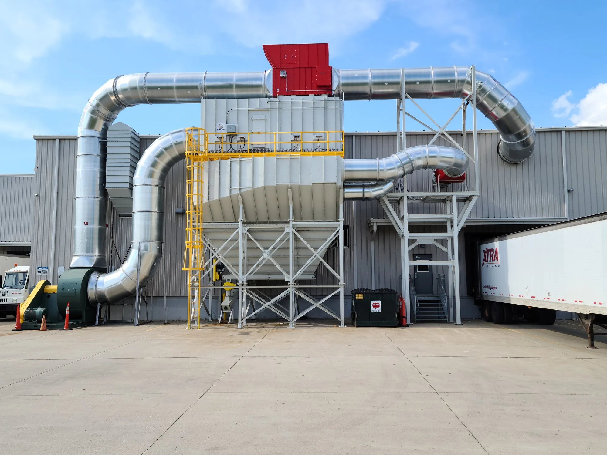 A large fabric-filter collector outside a plant, ducting running to it and a red abort gate on top, trailer at the dock.